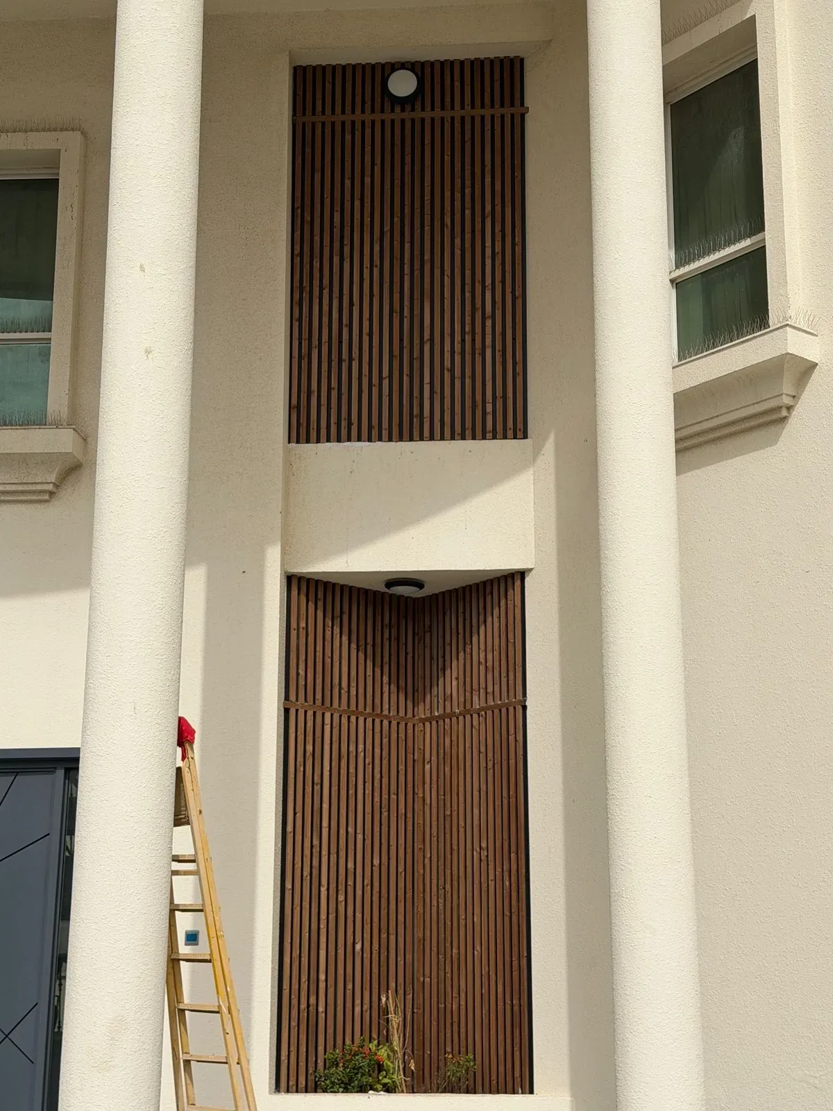 Two recessed entrance niches between columns, clad in dark slatted exterior panels with downlights